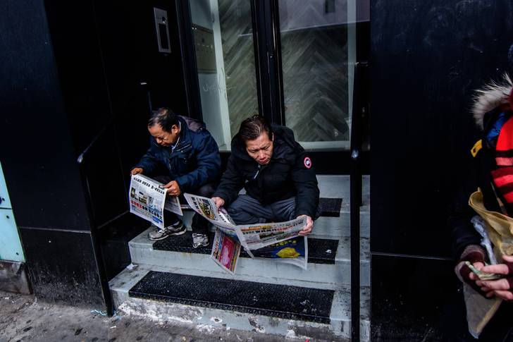 A photo of people reading newspapers on a stoop in Chinatown